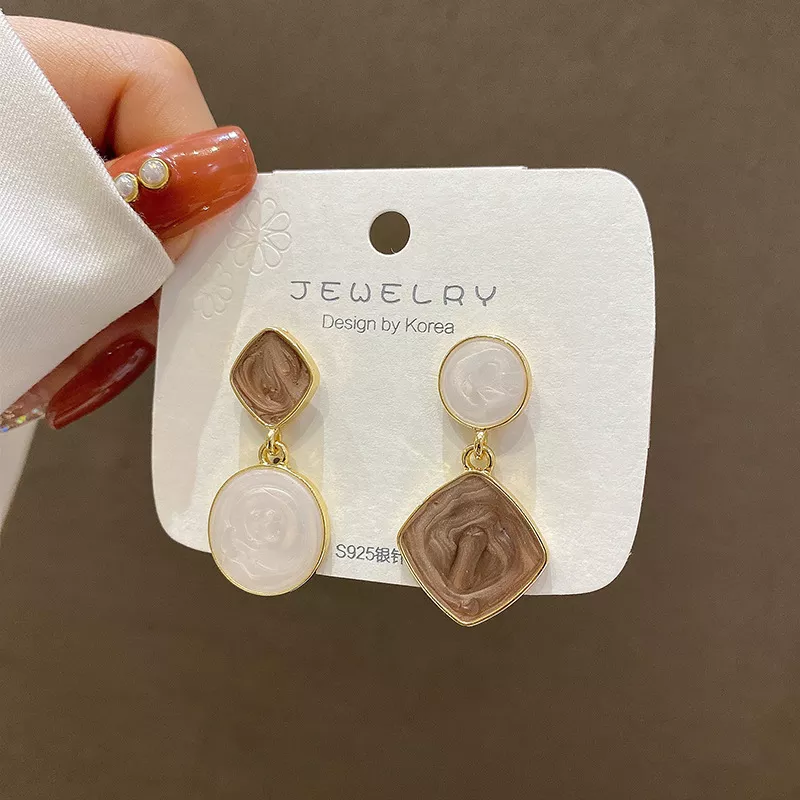 Une main tenant une paire boucles d'oreilles dépareillées tendance bleues et bleu ciel .