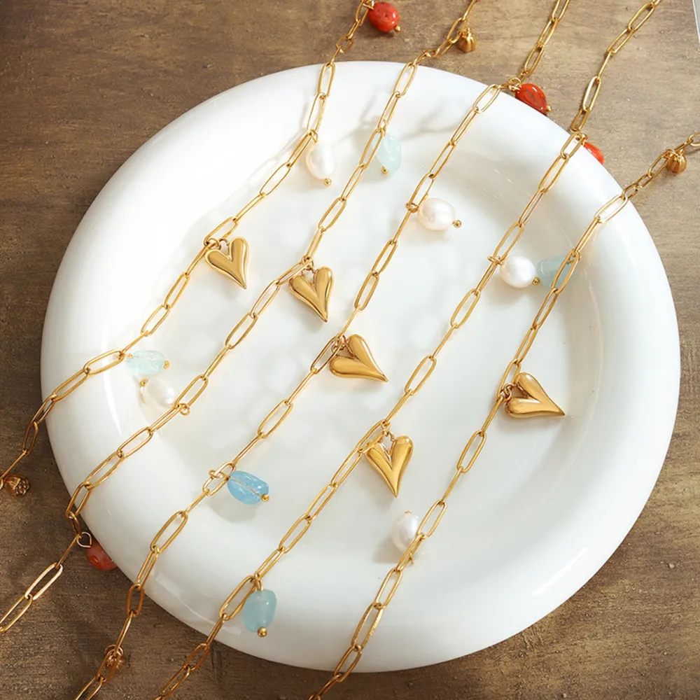 Cinq colliers en chaîne dorée avec des pendentifs en forme de cœur, des perles de couleur et des perles sont disposés sur une assiette blanche posée sur une surface en bois.