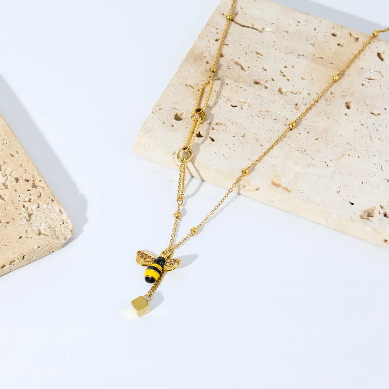 Un collier pendentif Abeille en Acier Inoxydable Doré posé sur une pierre.