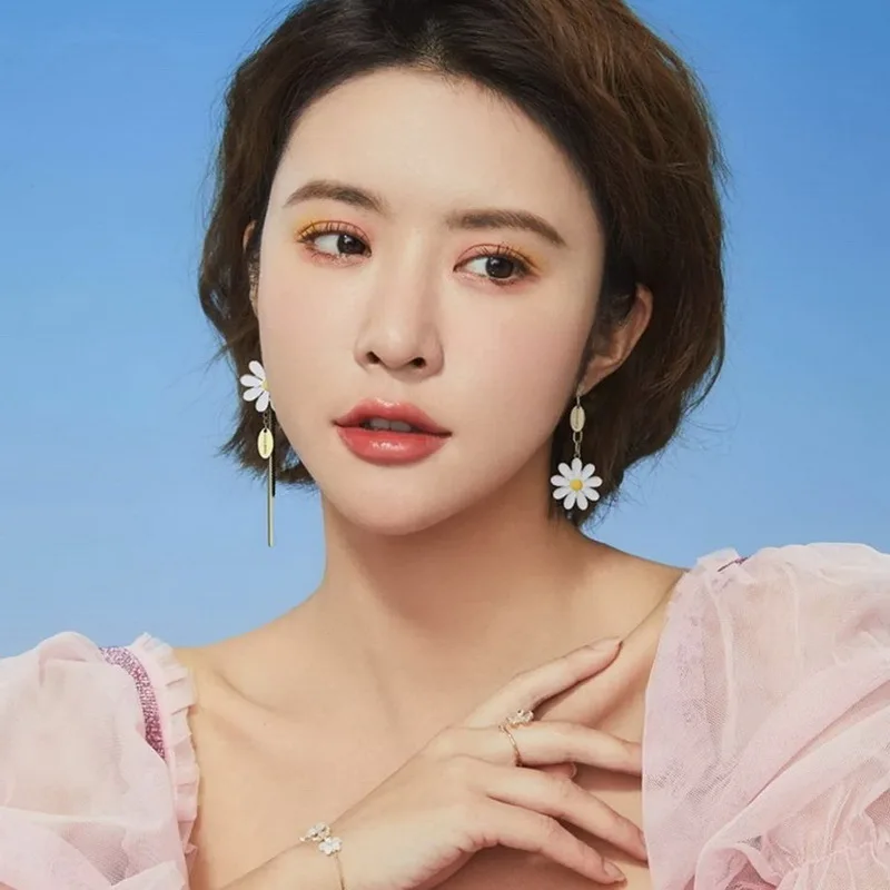 Une femme au cheveux court portant une robe rose avec des boucles d'oreilles en forme de marguerite, dite Boucle d'Oreille Asymétrique fleur.