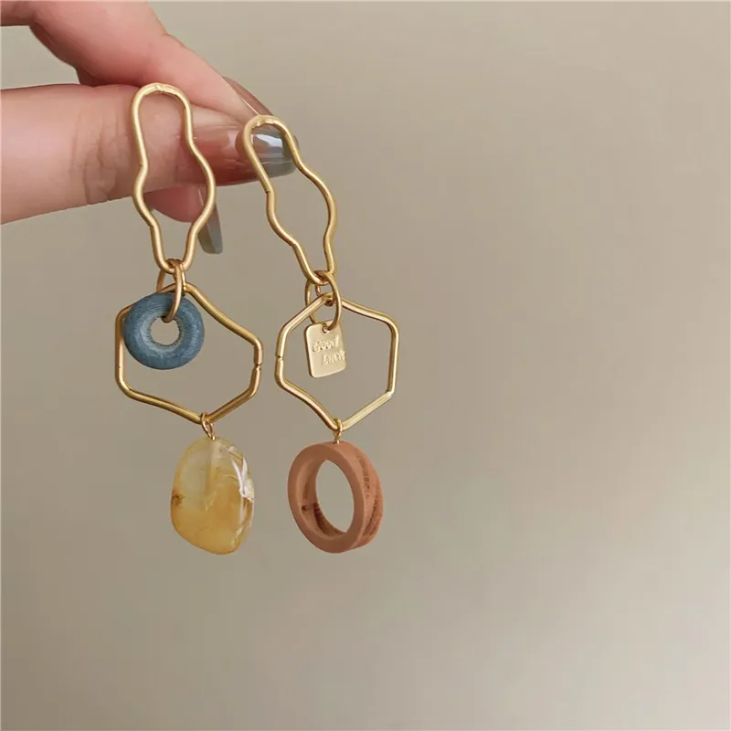 Une personne tenant une Boucle d'Oreille Dépareillée Doré Abstrait avec une pierre bleue et jaune, présentant un dessin abstrait.