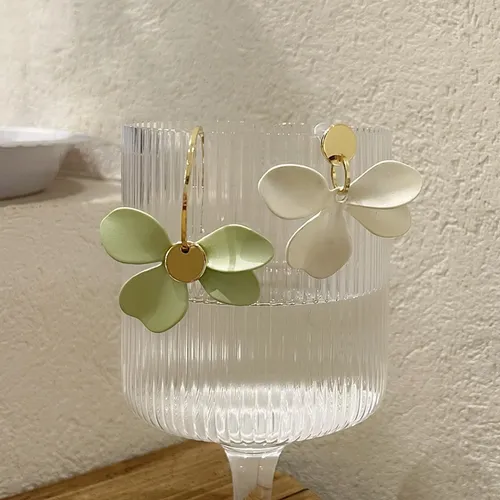 Une paire de Boucles d'oreilles asymétriques Pétales de Fleurs exposées sur un verre.