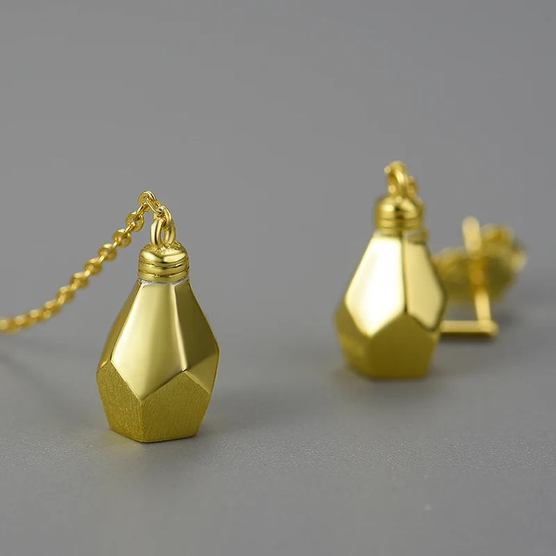 Une paire de boutons de manchette en or de forme géométrique, dont un avec une chaîne, présentés sur fond gris, évoquant le style moderne et artistique de la collection ROSY Boucles d'oreilles asymétriques goute.