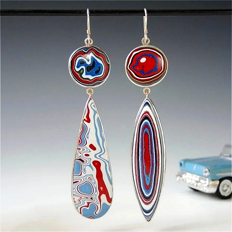 Paire de boucles d'oreilles dépareillées présentant des motifs abstraits en rouge, bleu, blanc et noir, avec un modèle réduit de voiture en arrière-plan.