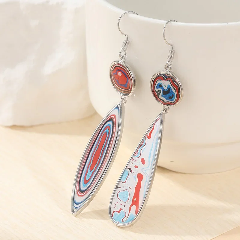 Deux boucles d'oreilles pendantes de forme ovale et en goutte d'eau allongée, présentant des motifs abstraits rouges, bleus et blancs, sur un fond neutre.